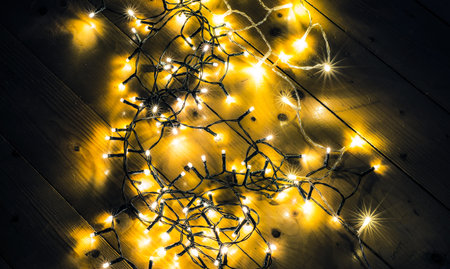 Warm, glowing Christmas string lights hanging above a rustic wooden background. Ideal for holiday banners, festive designs, seasonal marketing, and cozy winter-themed projects.の写真素材
