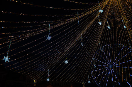 A wide-angle night photograph of a festive Christmas light canopy featuring golden and blue strands,...