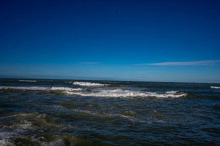 Dynamic ocean waves crashing under a clear blue sky, showcasing the power and movement of the sea. A...