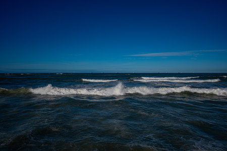 Dynamic ocean waves crashing under a clear blue sky, showcasing the power and movement of the sea. A clean and dramatic seascape ideal for travel, nature, wellness, and environmental design projects.の写真素材