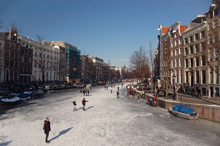 Wide angle view of pedestrians and skaters in the winter sun on a frozen canal in Amsterdam.のeditorial素材