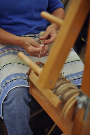 A woman's hands making yarn with a traditional spinning wheel.