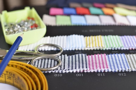 Close-up view view of a pair of scissors, a pencil on top of a tape measure, needles in a box,...
