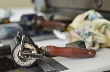 An ink roll with a pale red handle covered with black ink used for a manual letterpress print machine, on a table, in front of dirty cleaning clothの写真素材