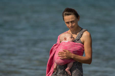A beautiful young mom with an infant daughter in a wrap.の写真素材