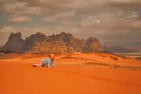 A cute baby girl crawling on a sand. Wadi Rum desert and mountains, Jordan.の写真素材