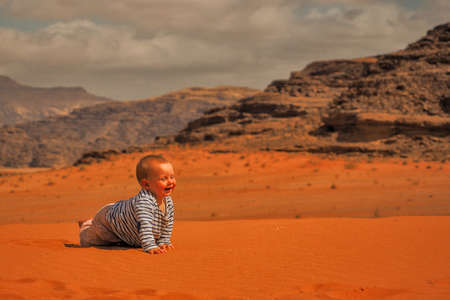 A cute baby girl crawling on a sand. Wadi Rum desert and mountains, Jordan.の写真素材