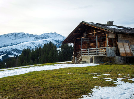 beautiful alpine landscape with wooden house and snowy mountains in backgroundの写真素材
