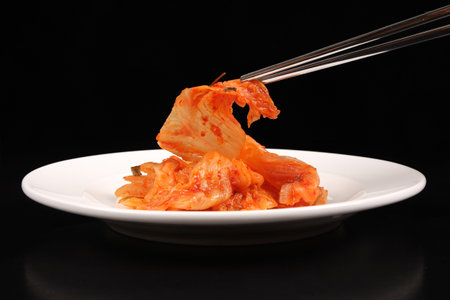 Chopsticks holding kimchi against black backgroundの写真素材