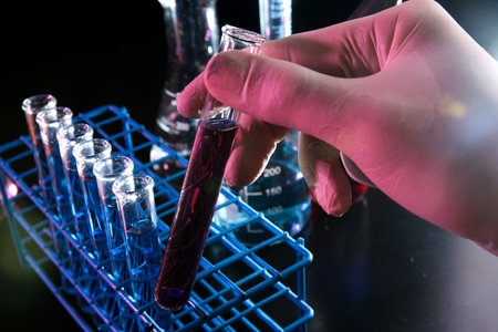Hand holding test tube containing red reagent in dark lab