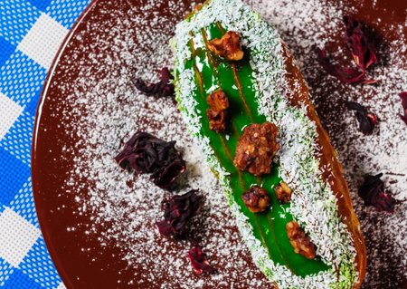 Tasty green pistachio eclair with coconut flakes serving on a brown plate