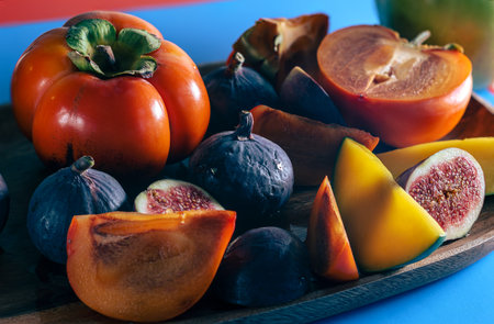 Persimmon, mango and figs on a wooden tray side view on blue