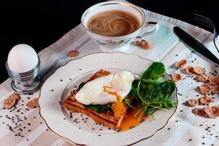 Healthy breakfast with poached egg on toast with green salad leaves. Egg yolk spread