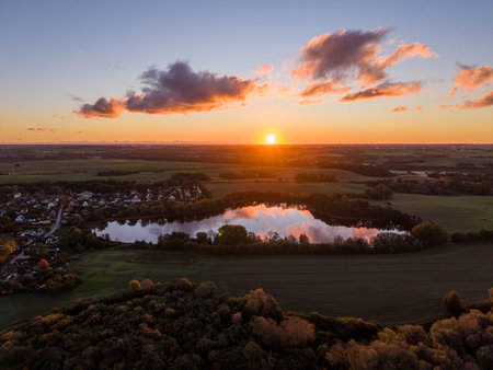 calm lake mirrors the vivid colors of a dramatic sunset sky, surrounded by open fields and a quiet village nestled in the peaceful countryside, Sildemow near Rostockの写真素材
