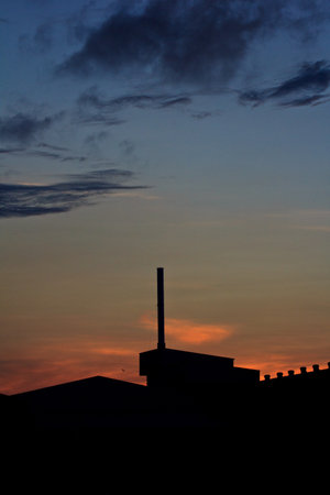 Landscape of sunrise with orange sky and the silhouette of a small factory の写真素材