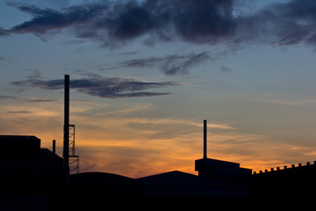 Landscape of sunrise with orange sky and the silhouette of a small factory の写真素材