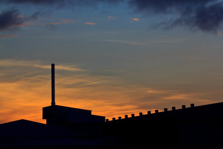 Landscape of sunrise with orange sky and the silhouette of a small factory の写真素材