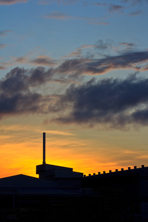 Landscape of sunrise with orange sky and the silhouette of a small factory の写真素材