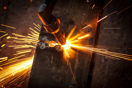 Welder in workshop manufacturing metal construction by cutting to shape using huge orange sparks