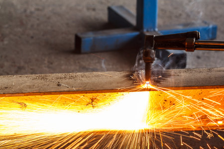 Welder in workshop manufacturing metal construction by cutting to shape using huge orange sparks