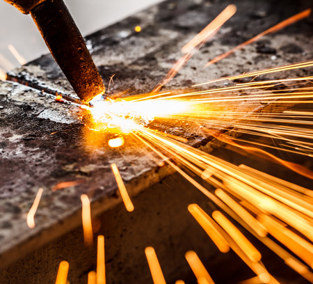 Welder in workshop manufacturing metal construction by cutting to shape using huge orange sparksの写真素材