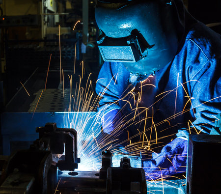 Welder working a welding metal with protective mask and sparksの写真素材