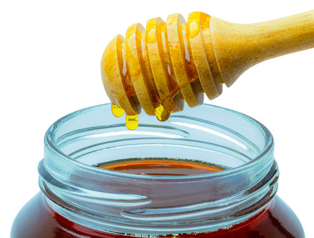 Honey dripping from a honey dipper in a glass cupの写真素材