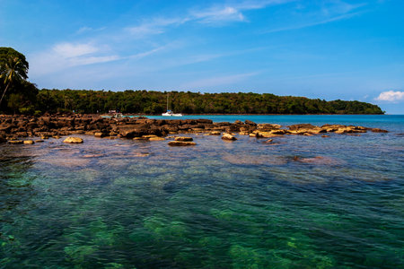 Rocks under  crystal clear sea water in foreground, yacht in green color sea water in middle and blue sky in backgroundの写真素材