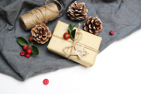 Christmas festive styled stock image composition. Handmade Christmas gift box, red berries, pine cones isolated on grey linen blanket. Flat lay, top view. Winter holiday background. Winter concept.の写真素材