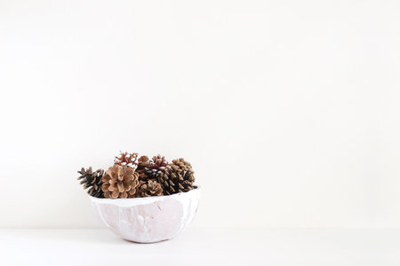Pinecones in ceramic bowl on white table. Christmas styled stock photo, holiday background.の写真素材