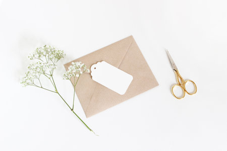 White gift tag with craft paper envelope, golden scissors and babys breath Gypsophila flowers isolated on white table background. Wedding or birthday styled stock photo, top view, flat lay composition.の写真素材