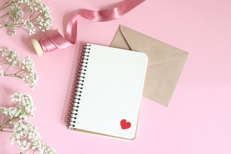 Wedding, birthday or Valentines stationery mockup. White babys breath Gypsophila flowers, satin ribbon, craft paper envelope and blank notebook, pink background.の写真素材