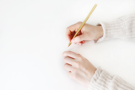 Womans hands in sweater holding golden balpoint pen ready writing, drawing isolated on white...