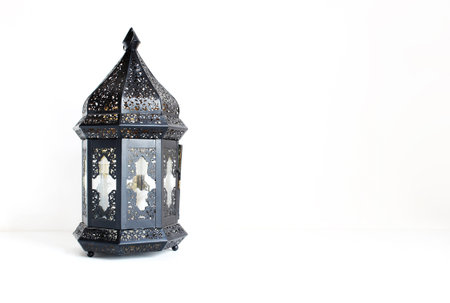 Ornamental dark Moroccan, Arabic lantern on the white table. Greeting card for Muslim community holy month Ramadan Kareem. Festive background with a lot of empty space.の写真素材