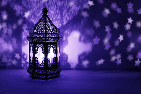 Ornamental Arabic lantern with burning candle glowing at night and glittering stars shaped bokeh lights. Festive greeting card, invitation for Muslim holy month Ramadan Kareem. Dark background.の写真素材