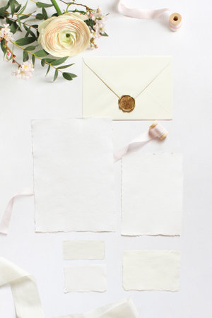 Feminine wedding, birthday desktop mock-ups. Blank greeting cards, envelope. Eucalyptus branches, pink cherry tree blossoms and Persian buttercup flowers. White table background. Flat lay, top view.の写真素材