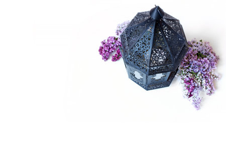 Ornamental dark Moroccan, Arab lantern with lilac flowers on the white table. Greeting card for...