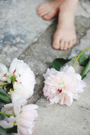 Feminine styled stock photo. Vertical composition. White and pink peony flowers on grunge concrete floor. Defocused kids bare foots in the background.の写真素材