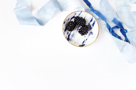 Feminine wedding or summer table composition. Porcelain plate with blackberry fruit and blue silk...