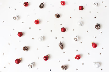 Christmas styled composition. Red Christmas glass balls, baubles, silver confetti stars and larch cones on white table background. Flat lay, top view. Decorative winter patternの写真素材