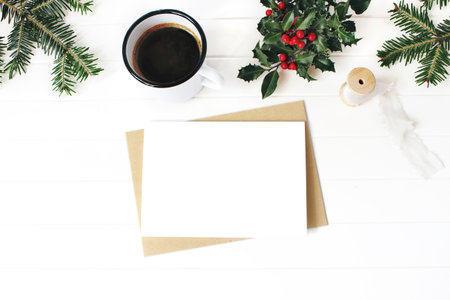 Christmas composition. Cup of coffee, holly berries, fir Christmas tree branches and silk ribbon on white wooden table background. Decorative frame. Winter holiday concept. Flat lay, top viewの写真素材