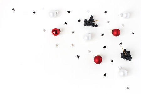 Christmas composition. Red and white Christmas glass balls, baubles, silver confetti stars and black privet, Ligustrum berries on white table background. Flat lay, top view. Decorative winter pattern.の写真素材