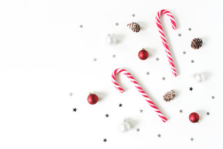 Christmas styled composition. Christmas red and white balls, baubles, candy canes, glittering silver stars confetti decoration and larch cones on white background. Flat lay, top view. Winter patttern.の写真素材