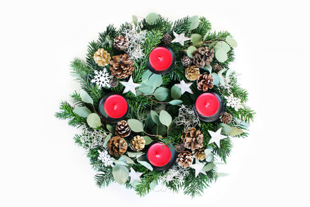 Christmas advent wreath isolated on white table background. Decorated by evergreen fir tree branches, eucalyptus leaves, snowflakes, golden and natural pine cones and red candles. Flat lay, top view.の写真素材