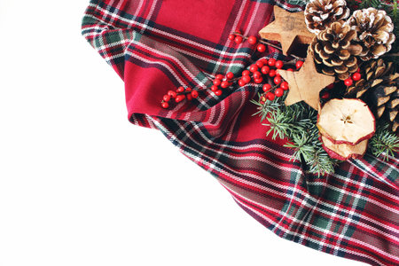 Christmas festive styled composition. Winter floral arrangement. Pine cones, fir tree branches, red holly berries and wooden stars and on checkered tartan plaid. White table background. Flat lay, topの写真素材