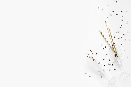 Happy New Year composition. Champagne glasses with golden confetti stars and drinking straws isolated on white table background. Celebration, party concept. Flat lay, top view. Empty copy space.の写真素材
