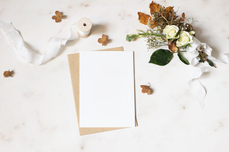 Feminine winter wedding, birthday stationery mock-up scene. Blank greeting card, envelope. Dry hydrangea, white roses and gypsophila flowers bouquet. Marble stone table background. Flat lay, top view.の写真素材