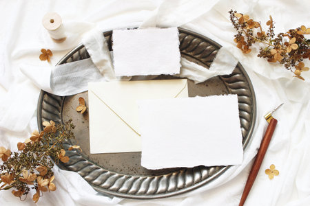 Styled stock photo. Winter, fall wedding, birthday table composition. Stationery mockup scene. Greeting cards, envelope, dry hydrangea flowers and calligraphy pen on silver tray. Flat lay, top view.の写真素材