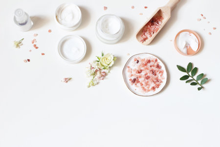 Styled beauty frame, web banner. Skin cream, tonicum bottle, dry flowers, leaves, rose and Himalayan salt. White table background. Organic cosmetics, spa concept. Empty space, flat lay, top view.の写真素材