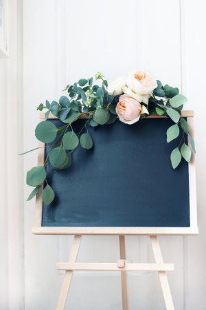 Empty wedding chalkboard sign mockup scene. Floral garland of eucalyptus branches and apricot English roses flowers. Rustic birthday party decoration. Wooden easel with welcome board. Vertical.の写真素材
